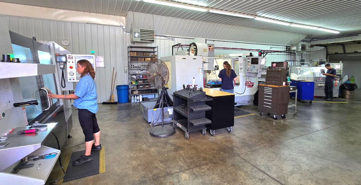 Three people working on creating parts in a machine shop.